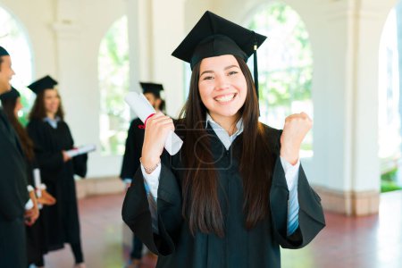 Téléchargez les photos : Caucasienne magnifique femme se sentant excitée de terminer ses études collégiales portant sa robe de graduation et casquette - en image libre de droit