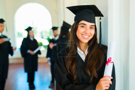 Téléchargez les photos : Belle femme hispanique souriante faisant contact visuel après avoir obtenu son diplôme universitaire lors d'une cérémonie de remise des diplômes sur le campus - en image libre de droit
