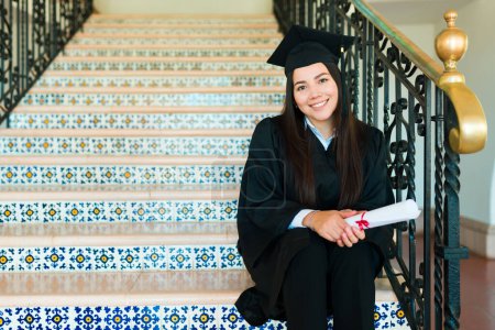 Photo for Caucasian attractive woman smiling sitting on the college stair after getting her diploma during graduation ceremony - Royalty Free Image