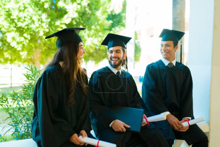 Photo for Cheerful latin man smiling while talking with his friends during the graduation ceremony on college campus - Royalty Free Image
