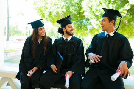 Photo for Hispanic young graduates chatting looking happy while sitting together after their graduation ceremony - Royalty Free Image