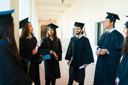 Téléchargez les photos : Groupe d'amis diplômés bavarder sur le campus du collège après avoir obtenu leur diplôme universitaire après la cérémonie de remise des diplômes - en image libre de droit