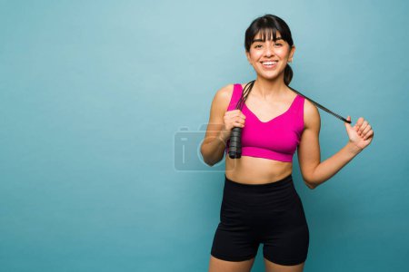 Téléchargez les photos : Joyeux latino jeune femme souriante et prête à commencer à sauter la corde et l'exercice avec une séance d'entraînement cardio - en image libre de droit