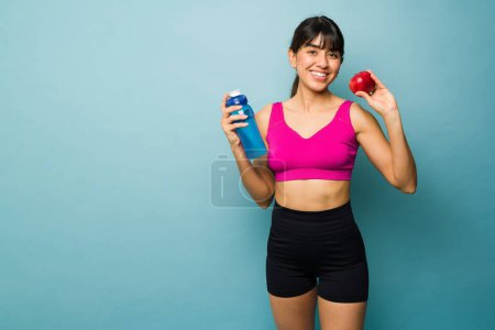 Téléchargez les photos : Athletic sporty woman on a diet eating an apple and drinking water before starting her exercise workout next to copy space - en image libre de droit