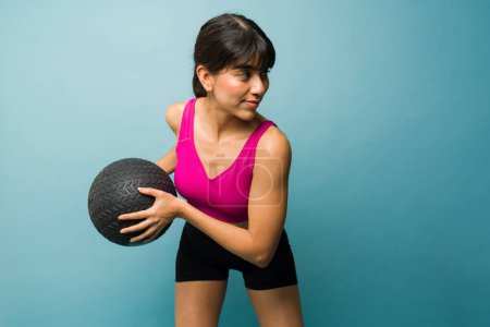 Photo for Latin fit young woman exercising with a cross training workout while using a slam ball in front of a studio background - Royalty Free Image
