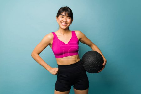 Téléchargez les photos : Magnifique femme active avec un corps athlétique souriant regardant heureux tenant une boule de slam pour son entraînement cross - en image libre de droit