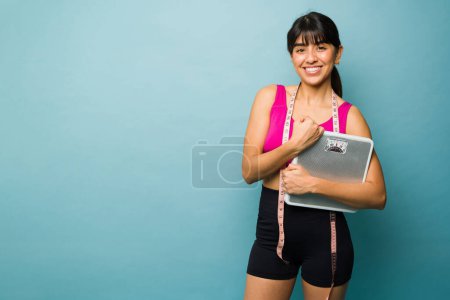 Téléchargez les photos : Belle femme heureuse utilisant une balance souriant heureux de perdre du poids et sa routine d'entraînement à côté de copier l'espace - en image libre de droit