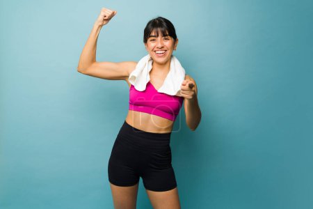 Téléchargez les photos : Gai femme forte avec un corps athlétique montrant son muscle biceps à l'aide d'une serviette de gym après son entraînement - en image libre de droit