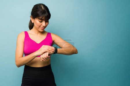 Téléchargez les photos : Fit young woman in sportswear looking at her smartwatch getting ready to start her run or workout against a copy space background - en image libre de droit