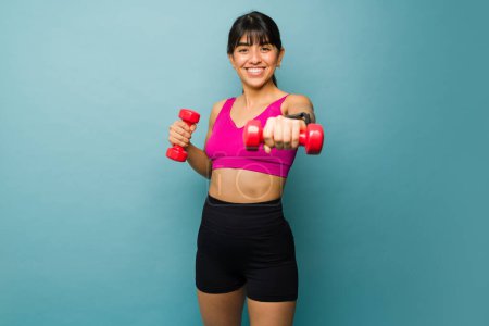 Photo for Cheerful beautiful woman in activewear exercising with a cardio workout using dumbbell weights and having fun - Royalty Free Image