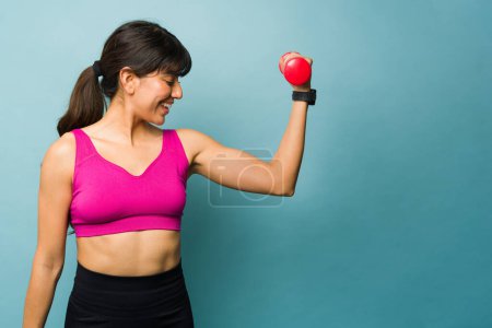 Foto de Sonriendo mujer fitness buscando feliz mientras levantando pesas de mancuerna haciendo rizos de bíceps sensación fuerte - Imagen libre de derechos