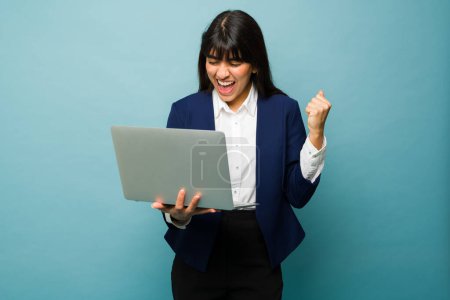 Foto de Mujer profesional emocionada celebrando el éxito de su negocio en línea o recibir buenas noticias mientras trabaja en el ordenador portátil - Imagen libre de derechos
