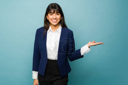Foto de Gorgeous professional woman showing a new product in her hand wearing a business suit against a studio background - Imagen libre de derechos