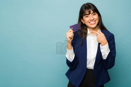 Téléchargez les photos : Femme d'affaires souriant et pointant vers sa nouvelle carte de crédit regardant professionnel sur un fond bleu avec espace de copie - en image libre de droit