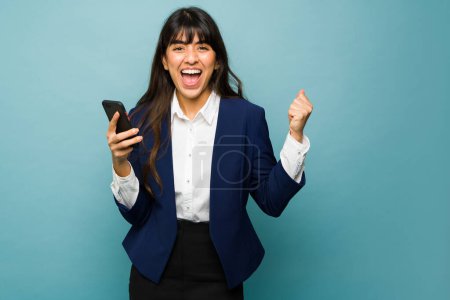 Téléchargez les photos : Cheerful business woman screaming with happiness and celebrating getting good news from work while using the smartphone - en image libre de droit