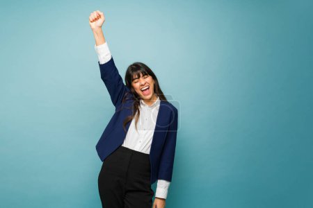 Photo for Hispanic young woman raising her arm and celebrating her successful business while working wearing a professional suit - Royalty Free Image