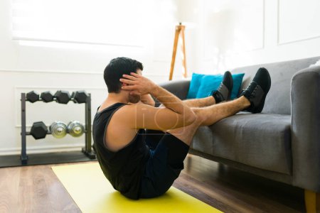 Téléchargez les photos : Side view of a fit young man working out at home and doing sit up exercises at his home gym - en image libre de droit