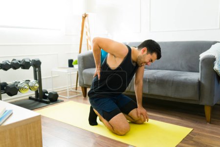 Photo for Stressed fit man suffering a back injury while doing workout exercises in the living room - Royalty Free Image