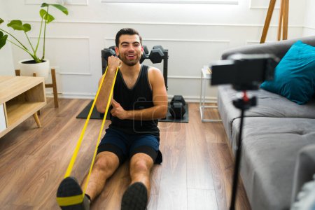 Photo for Attractive happy man filming a home workout video for his social media blog about fitness lifestyle - Royalty Free Image