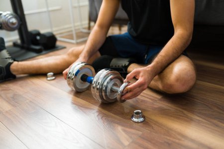 Téléchargez les photos : Close up of a young man sitting on the floor getting ready to exercise using dumbbell weights - en image libre de droit