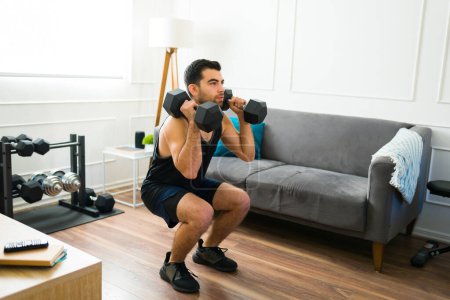 Téléchargez les photos : Strong fit man doing squat exercises while using dumbbell weights in his home workout - en image libre de droit