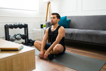 Foto de Hombre joven relajado haciendo una meditación o ejercicios de yoga después de un video de entrenamiento en casa - Imagen libre de derechos