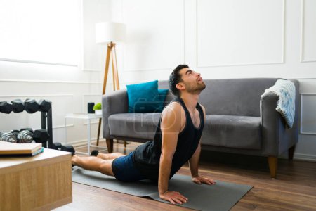 Photo for Fitness young man working out at home and training with a yoga workout doing a cobra pose - Royalty Free Image