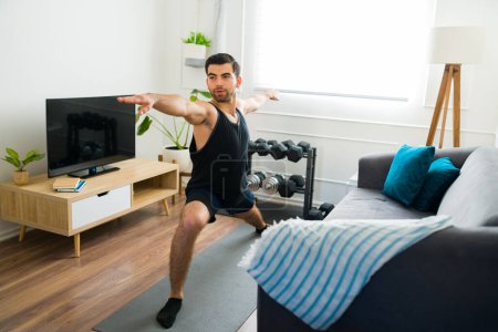 Téléchargez les photos : Determined young man with a lot of motivation practicing a warrior pose while exercising with a yoga workout - en image libre de droit