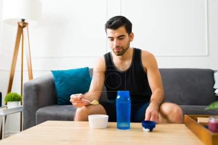 Photo for Attractive young man with a healthy fitness lifestyle at home preparing a protein shake to start his workout - Royalty Free Image