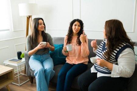Téléchargez les photos : Heureuses femmes détendues amis souriant et bavardant tout en buvant du café ensemble assis sur le canapé - en image libre de droit
