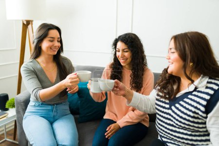 Foto de Happy young women and best friends drinking coffee while relaxing while chatting about gossip at home - Imagen libre de derechos