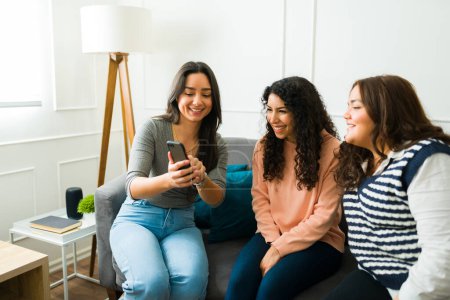 Foto de Happy young woman showing her text or social media on the smartphone to her excited best friends while chatting - Imagen libre de derechos
