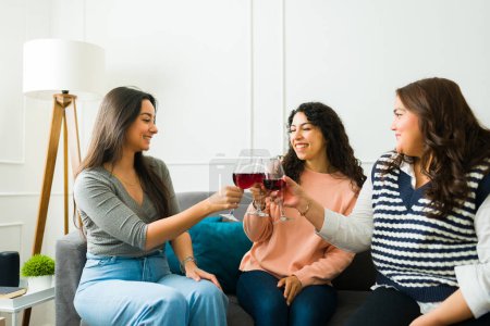 Foto de Beautiful happy women friends toasting while drinking wine and smiling having fun together at home - Imagen libre de derechos