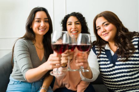 Photo for Cheerful young women and best friends saying cheers toasting while enjoying drinking a glass of wine together - Royalty Free Image