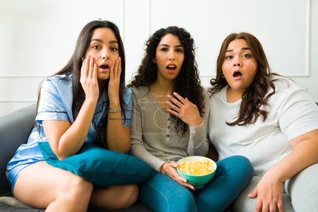 Foto de Surprised female friends looking shocked and screaming while watching a horror movie together during a sleepover - Imagen libre de derechos