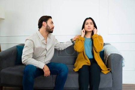 Téléchargez les photos : Femme hispanique agacée se disputant avec son mari tout en lui couvrant les oreilles et l'ignorant assis ensemble sur le canapé - en image libre de droit
