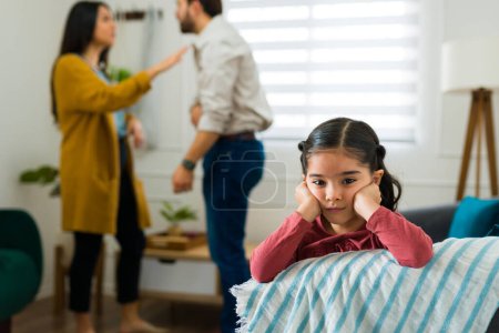 Schönes kleines Kind, das Augenkontakt herstellt, sieht traurig aus, während ihre Eltern vor einer Scheidung zu Hause streiten