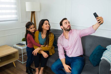 Photo for Caucasian father taking a selfie with his beautiful happy family while sitting together on the sofa in the living room - Royalty Free Image