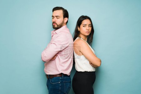Photo for Profile of an angry young woman and man turning their backs after a fight standing against a blue studio background - Royalty Free Image