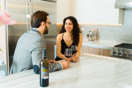 Téléchargez les photos : Joyeux beau couple souriant et parlant lors d'une date formelle à la maison tout en prenant un verre de vin ensemble - en image libre de droit