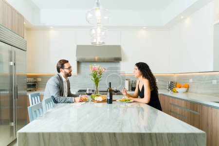 Photo for Profile of a romantic couple sitting at their granite kitchen island eating dinner during a formal date drinking wine - Royalty Free Image