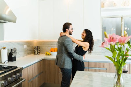 Téléchargez les photos : Heureux jeune couple étreignant et souriant après une date romantique formelle dans leur belle cuisine - en image libre de droit