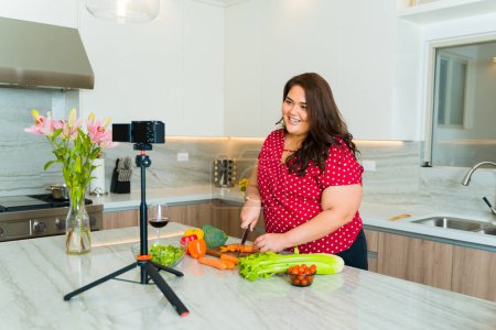 Téléchargez les photos : Blogueuse culinaire cuisiner le déjeuner tout en filmant une vidéo pour les médias sociaux dans sa belle grande cuisine blanche - en image libre de droit