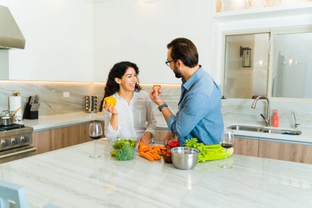 Téléchargez les photos : Joyeux jeune couple riant et s'amusant dans une cuisine de luxe blanche tout en cuisinant ensemble - en image libre de droit