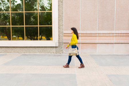 Foto de Perfil de una joven caminando llevando una bolsa de mensajería y viajando al trabajo en la ciudad - Imagen libre de derechos