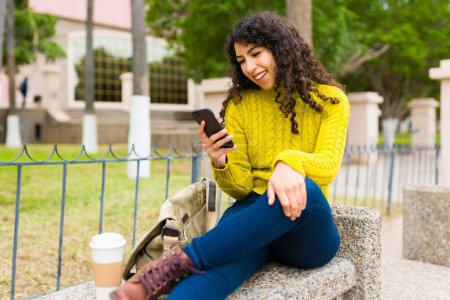 Photo for Cheerful caucasian woman laughing and having fun while texting or using social media on her smartphone while outdoors - Royalty Free Image