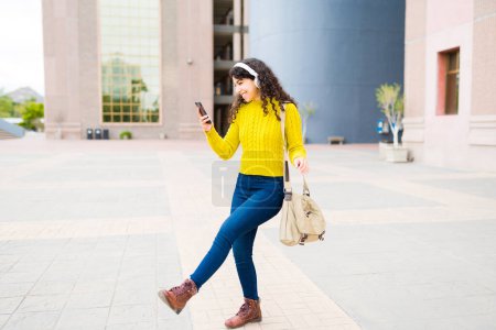 Foto de Longitud completa de una joven feliz divirtiéndose bailando mientras escucha música mientras camina por la ciudad y usa su teléfono inteligente - Imagen libre de derechos