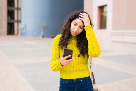 Foto de Mujer joven estresada sintiéndose perdida mientras busca direcciones en su teléfono inteligente utilizando los mapas GPS de la ciudad - Imagen libre de derechos