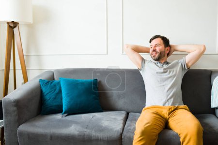 Photo for Happy attractive man looking relaxed while resting on the couch and relaxing in his beautiful living room home - Royalty Free Image