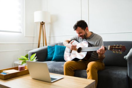 Photo for Handsome talented man playing the guitar and listening to music while relaxing during leisure time at home - Royalty Free Image